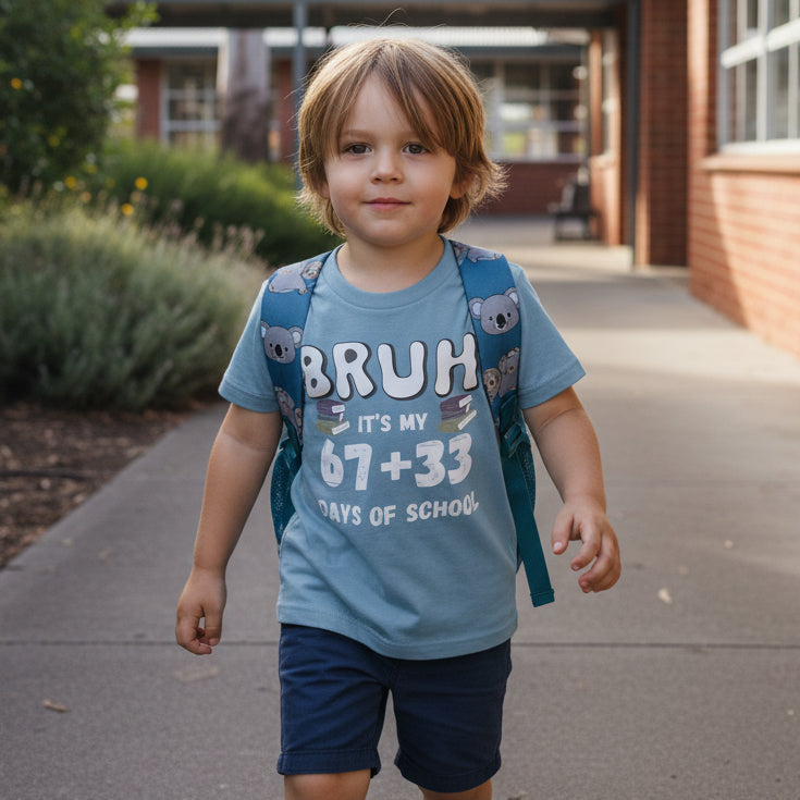 A light blue short-sleeve t-shirt with a graphic print that reads 'BRUH IT'S MY 67+33 DAYS OF SCHOOL' in white and gray lettering, displayed on a clean white background.