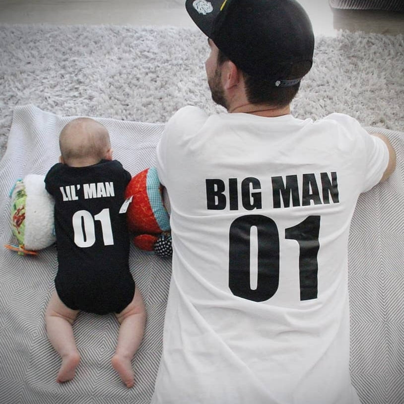 Dad and baby lying down in matching black and white garments with Big Man and Lil Man number designs on the back.