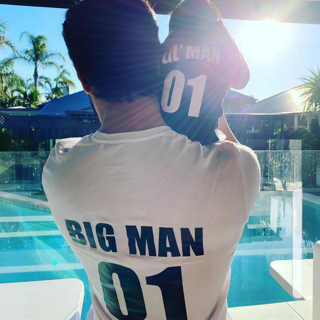 Two people wearing jerseys with 'BIG MAN 01' and "LIL' MAN 01' text by a poolside.