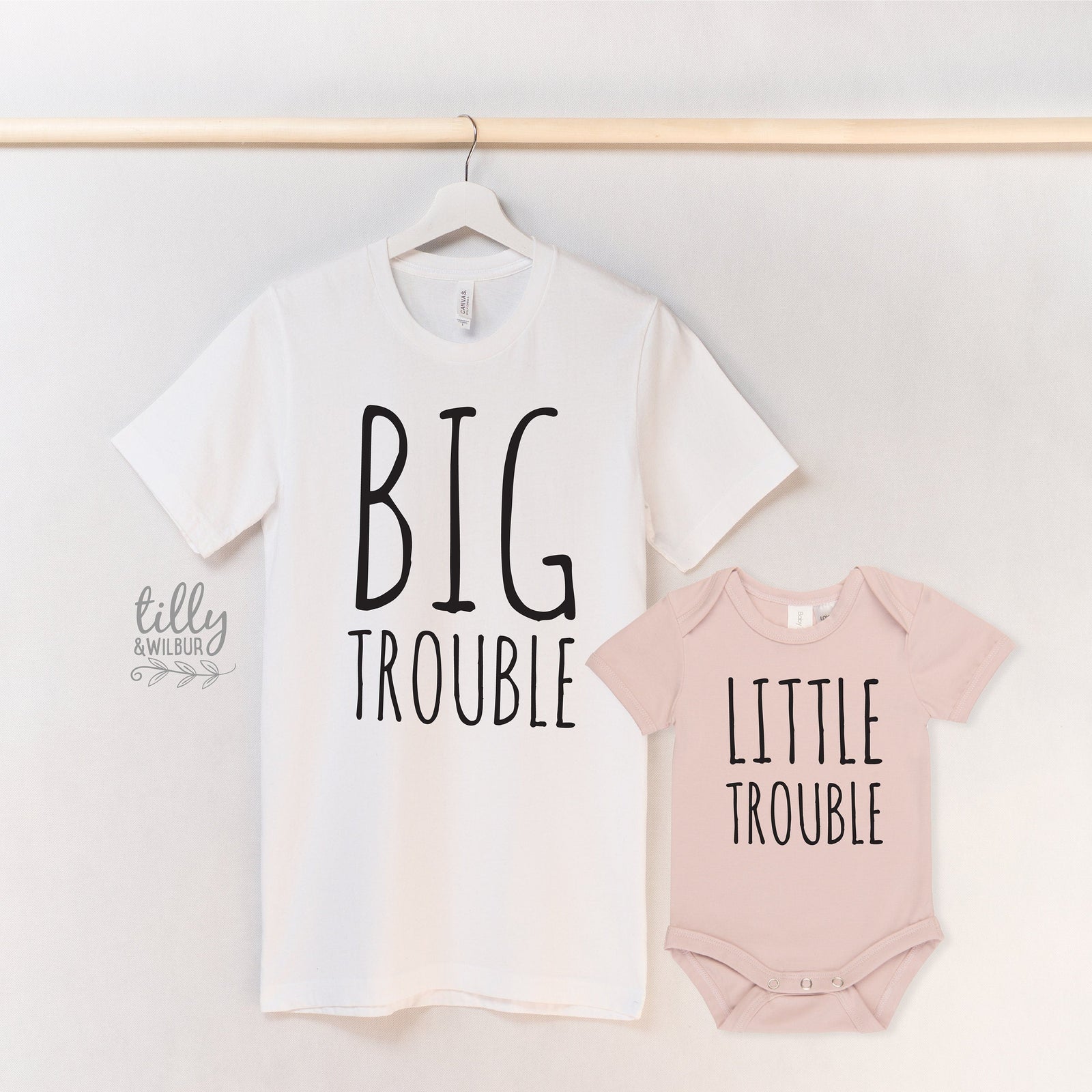 Man holding a child wearing a 'Little Trouble' outfit with a 'Big Troublemaker' shirt in a natural setting.