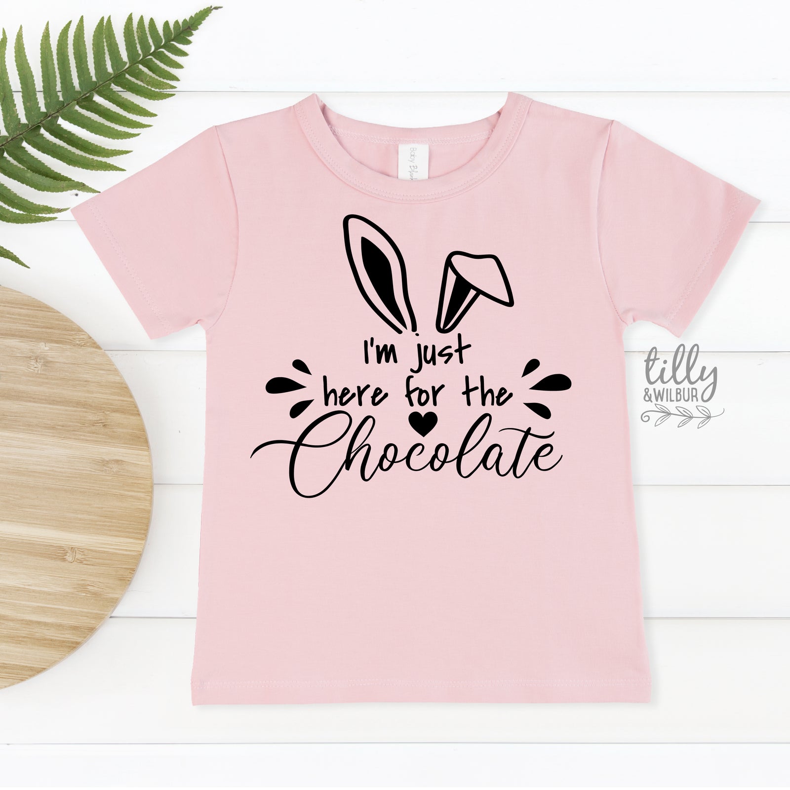 Pink t-shirt with bunny ears and text 'I'm just here for the chocolate' on a white background
