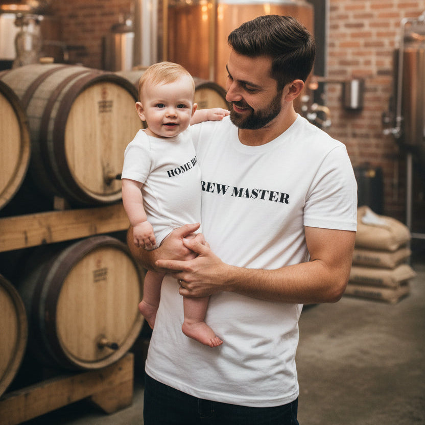 Dad and baby at a brewery in matching white tops that read Brew Master and Home Brewed.