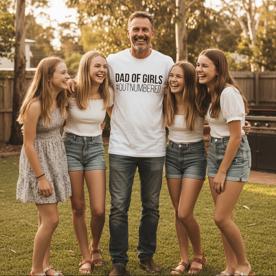 white t-shirt with bold white text reading Dad Of Girls #Outnumbered.