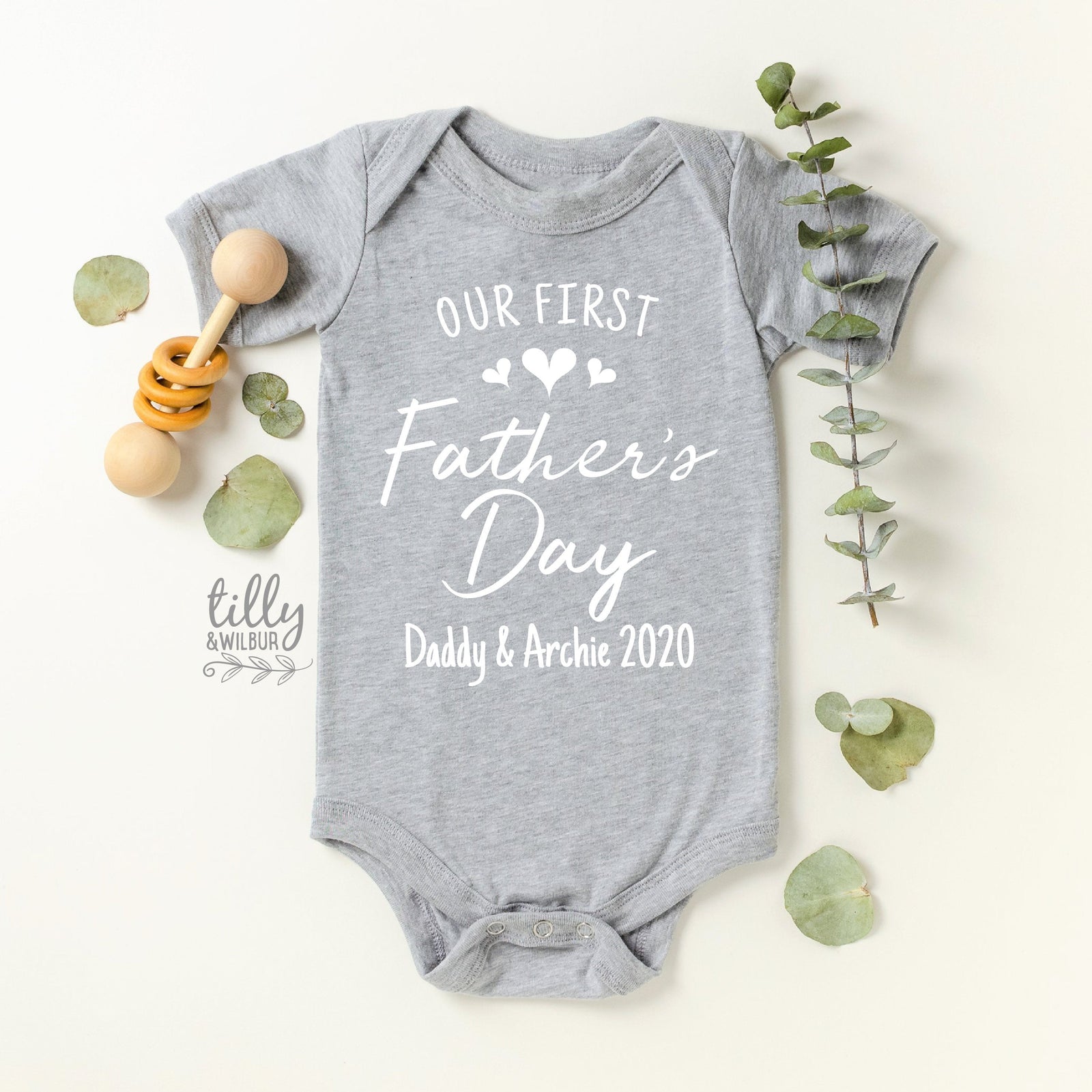 Grey short-sleeve baby bodysuit with Our First Father's Day script and personalised names and year.