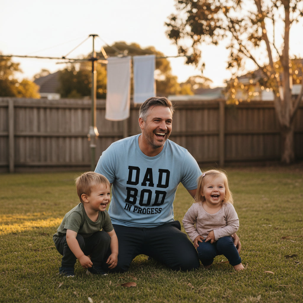Blue t-shirt reading Dad Bod In Progress in bold white varsity lettering.