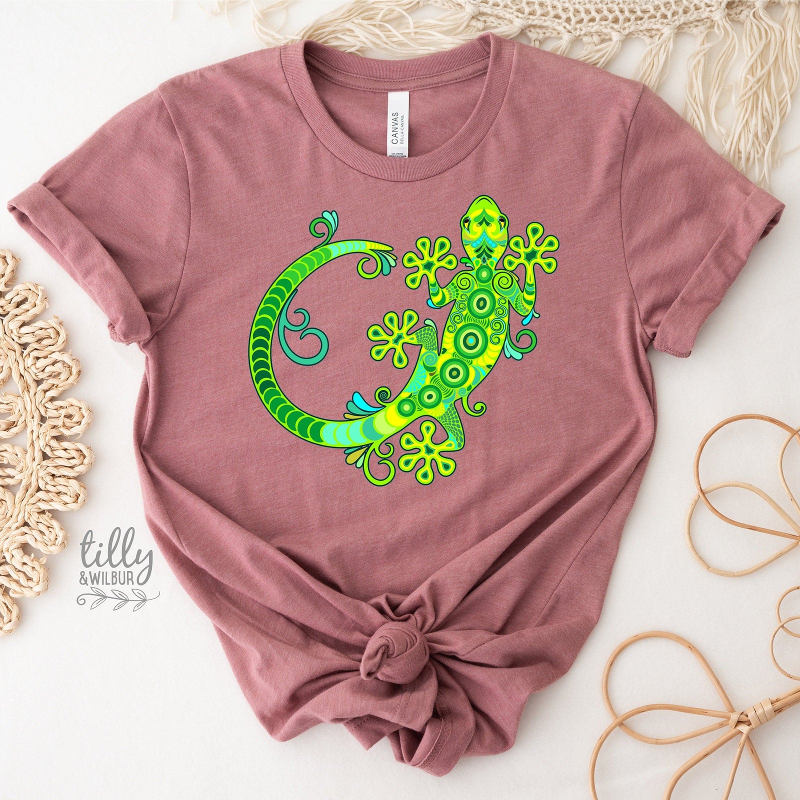 White t-shirt with a detailed vibrant green and turquoise decorative gecko illustration with swirling patterns