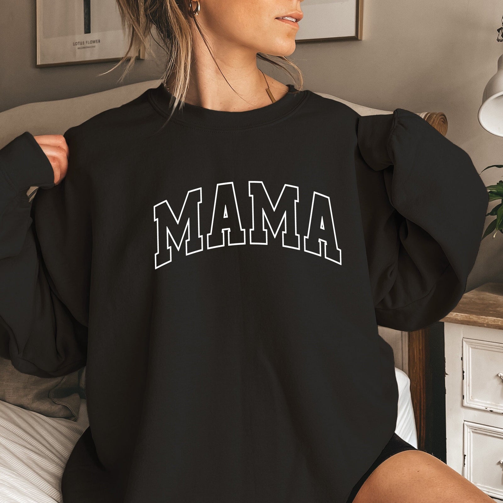 Person wearing a black sweatshirt with 'MAMA' text in a home setting