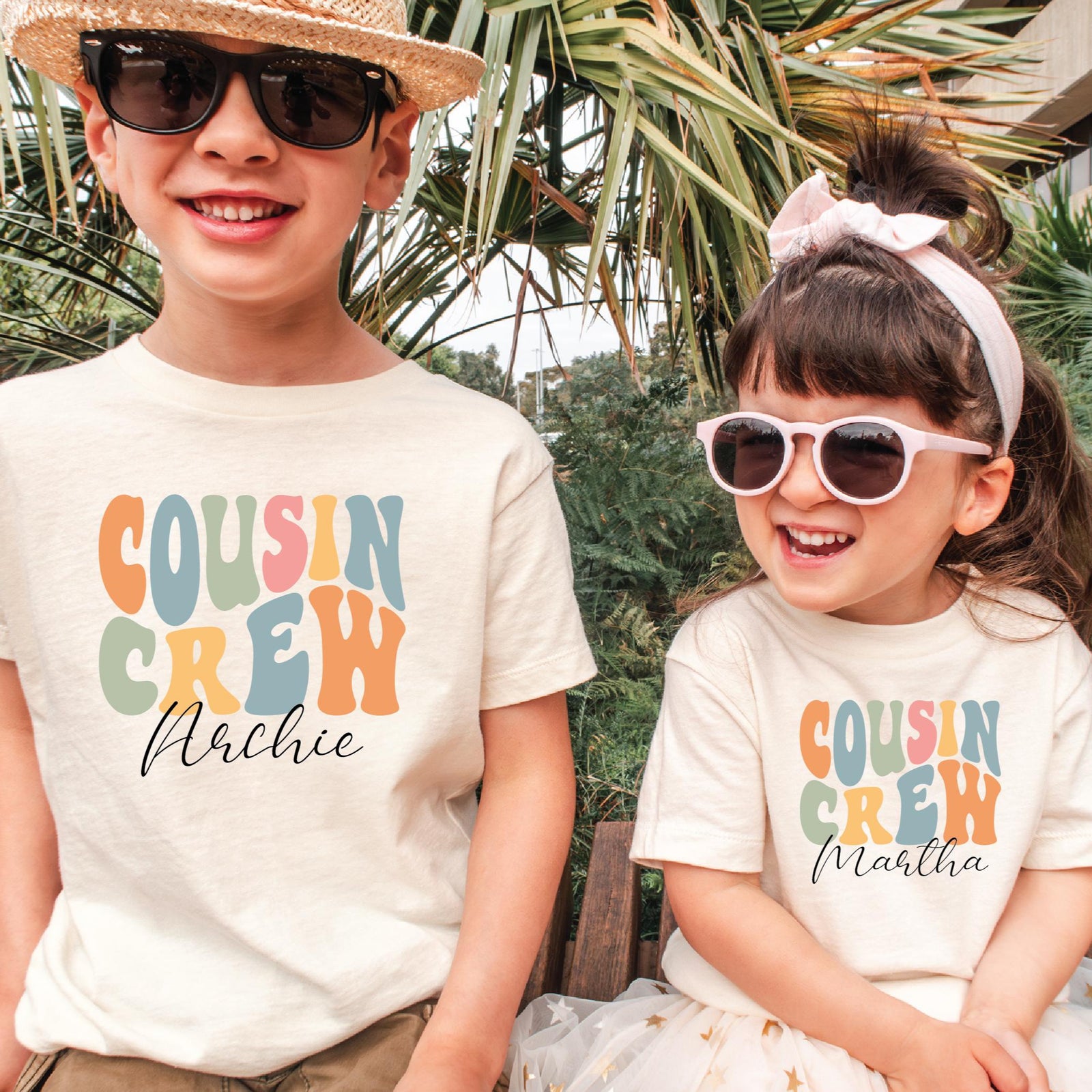 Two children wearing 'Cousin Crew' shirts with personalized names in a tropical setting.