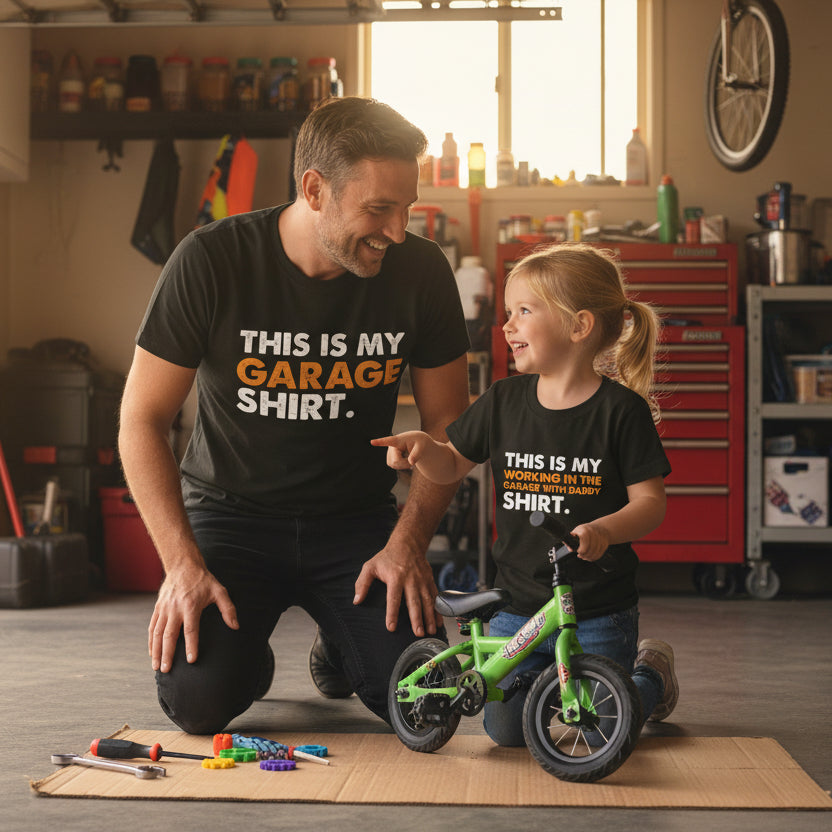 Two black t-shirts with text on a wooden surface, with an additional t-shirt in the background.
