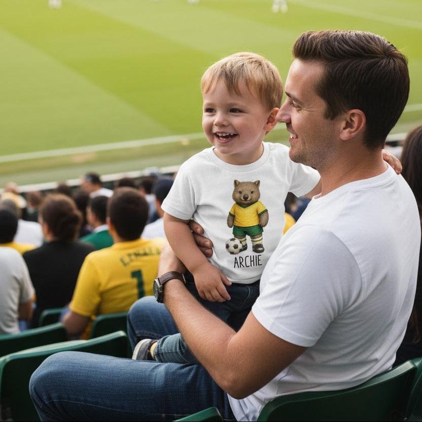 Tilly&Wilbur white kids tee printed with a green and gold wombat soccer player and a personalised name underneath.