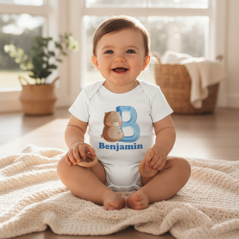 Bbay sitting on a blanket in a white bodysuit with a teddy bear initial and the name Benjamin.