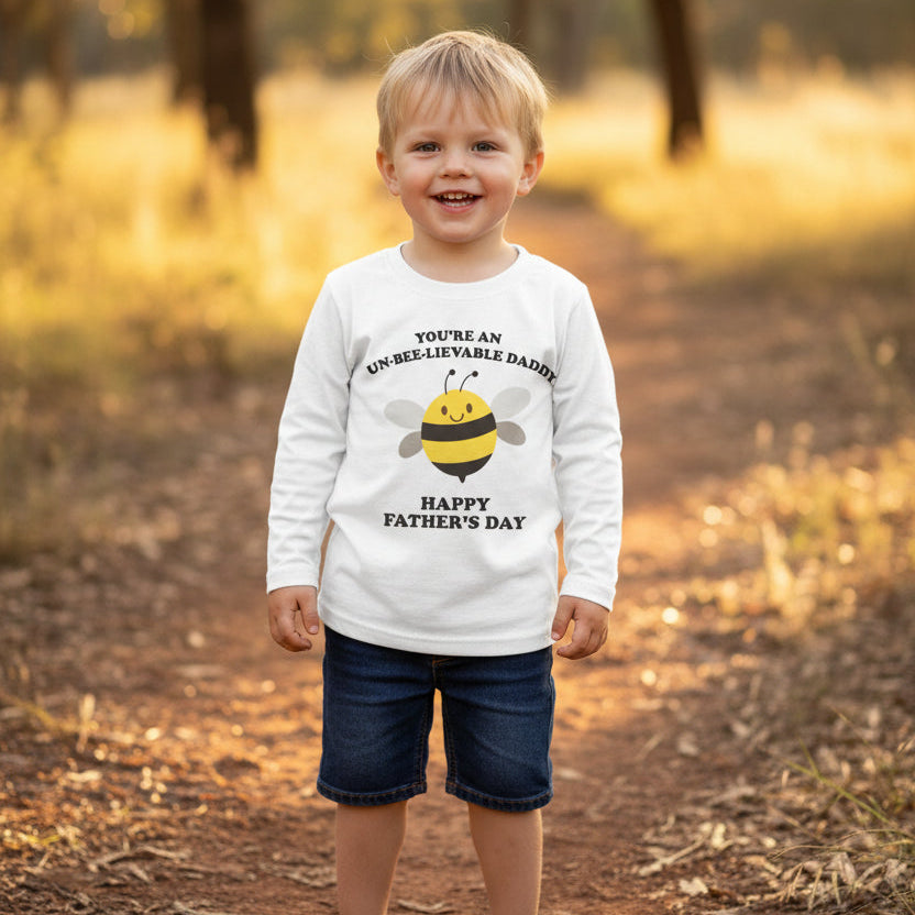 Toddler in a field wearing a white t-shirt with a cartoon bee reading You're An Un-Bee-Lievable Daddy, Happy Father's Day.