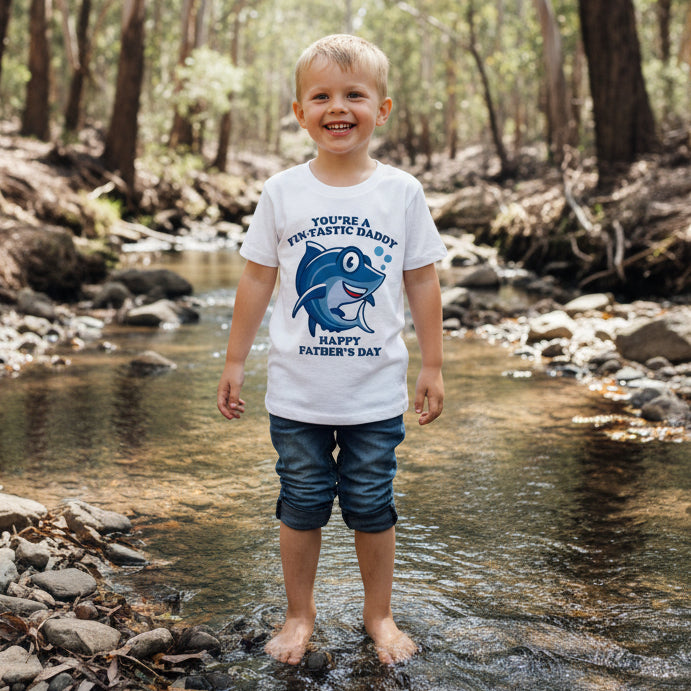boy wearing a white t-shirt with a cartoon shark reading You're A Fin-Tastic Daddy, Happy Father's Day.