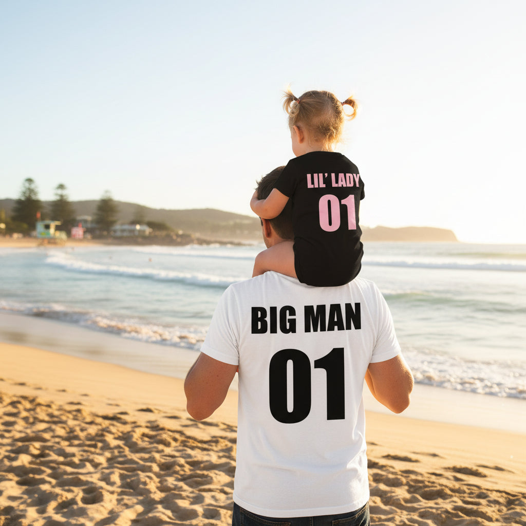 Dad at the beach carrying his daughter on his shoulders, wearing matching Big Man and Lil Lady number tops.