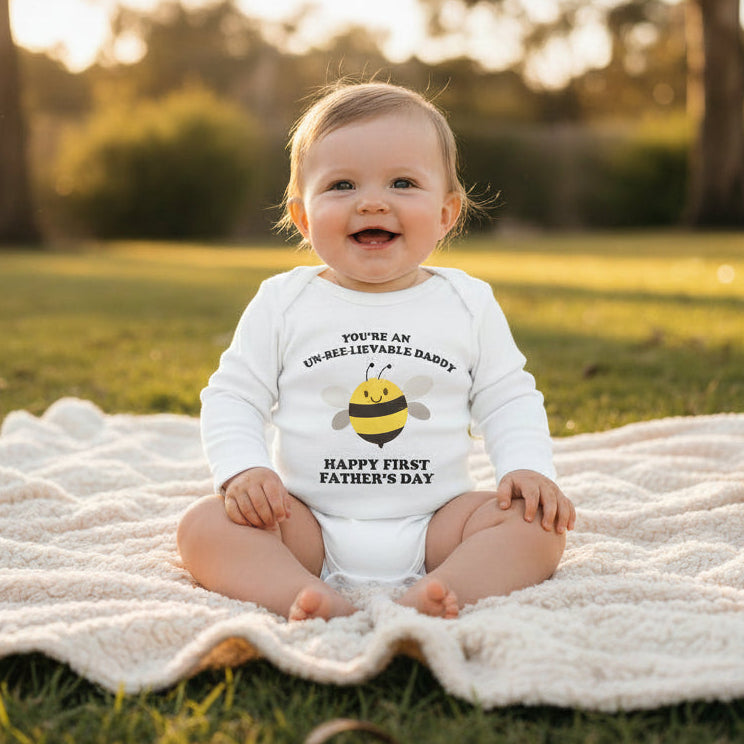 White baby bodysuit with a cartoon bee and text reading You're An Un-Bee-Lievable Daddy, Happy First Father's Day.