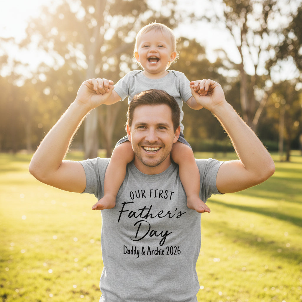 Dad carrying his baby on his shoulders, wearing a grey t-shirt that reads Our First Father's Day with a name and year.