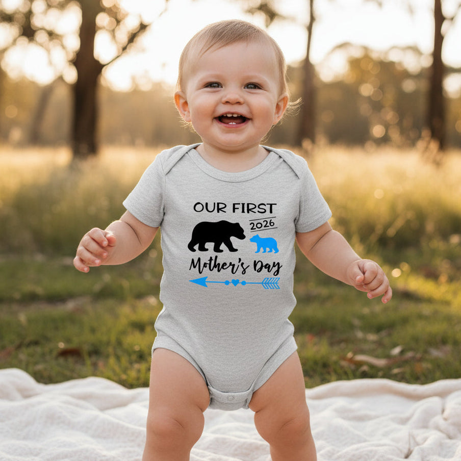 A grey baby bodysuit with 'Our First Mother's Day 2026' printed in black and blue, accompanied by silhouette illustrations of a mum bear and a baby bear