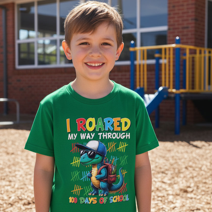 Child wearing a green t-shirt with a cartoon dinosaur in sunglasses and the words I Roared My Way Through 100 Days Of School.
