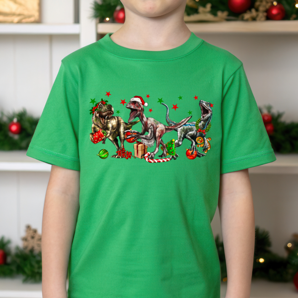Child wearing a green t-shirt with Christmas-themed dinosaur design in front of a decorated background.