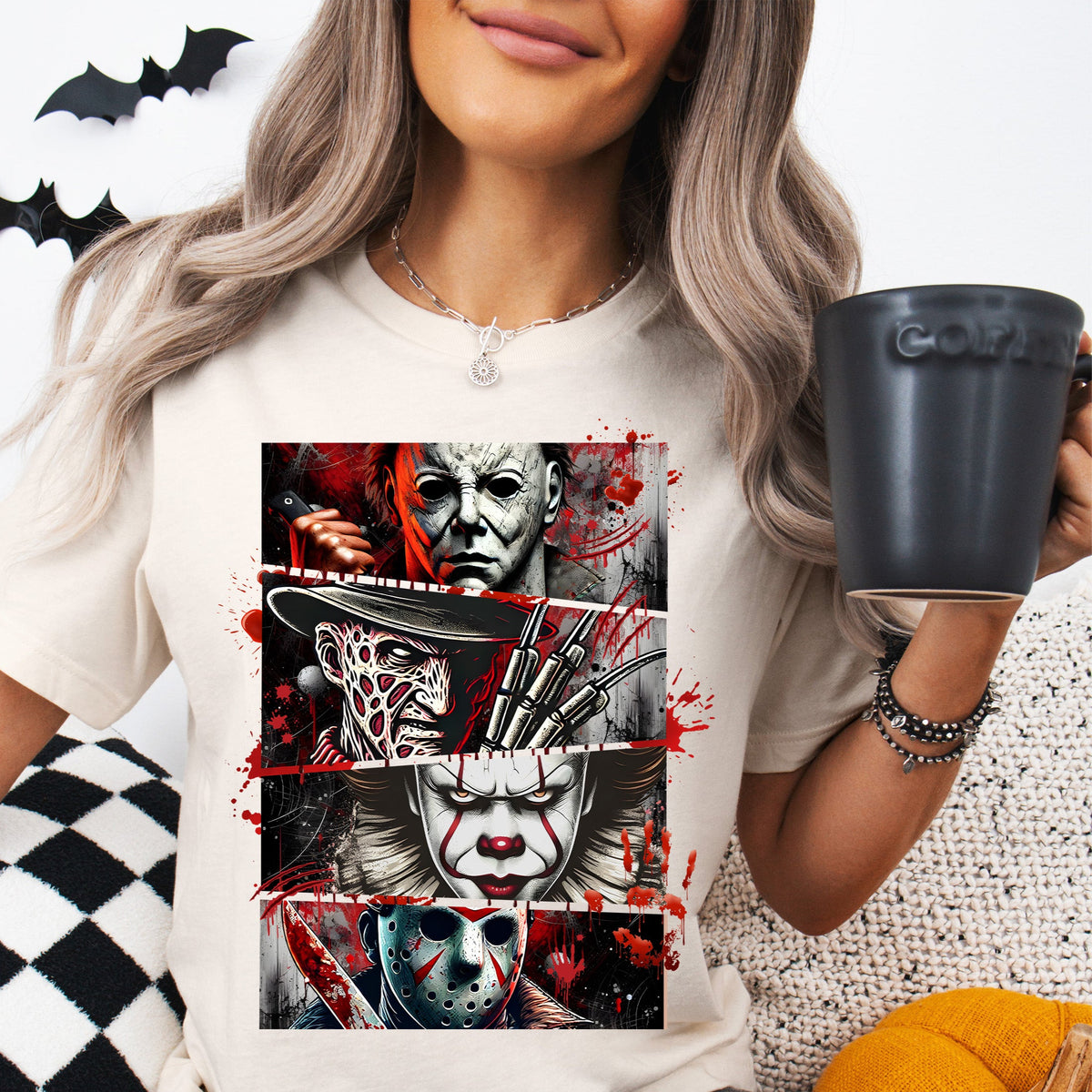 A person sitting and holding a coffee cup while wearing a t-shirt with a horror movie icon design.