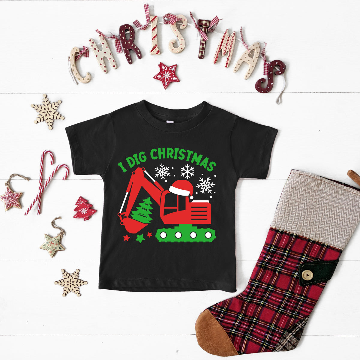 A black Christmas themed t-shirt with 'I Dig Christmas' text and a graphic of a digger excavator, accompanied by plaid leg warmers and decorative stars around.