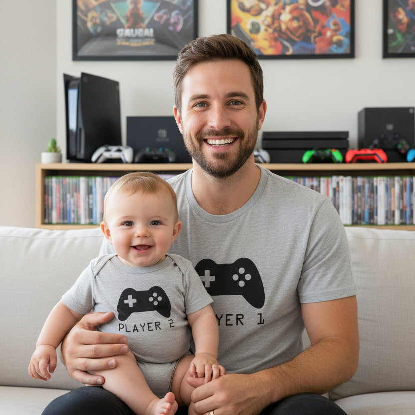 Dad and baby in matching grey tops with controller designs reading Player 1 and Player 2.