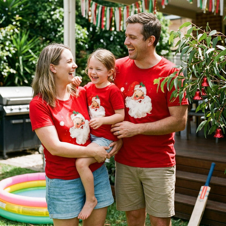 A red short-sleeve crewneck t-shirt featuring a vintage-style graphic of Santa Claus's face on the chest, complete with a white beard, red hat, and small green holly leaves.