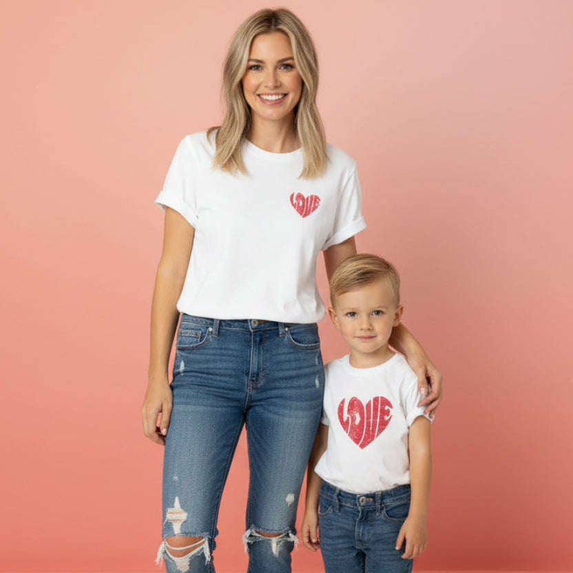 An adult and a child wearing matching white t-shirts with the word 'love' printed in red heart shape on the front.