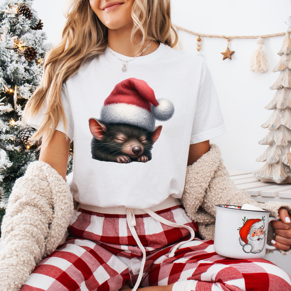 A person wearing a white t-shirt with a printed image of a Tasmanian Devil wearing a Santa hat, sitting in front of a Christmas tree and decorations.