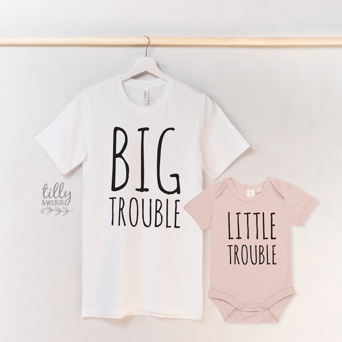 Man holding a child wearing a 'Little Trouble' outfit with a 'Big Troublemaker' shirt in a natural setting.