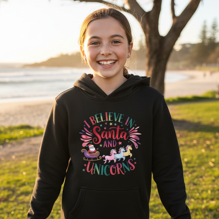 A black kids' pullover hoodie with a colorful graphic on the chest that reads 'I Believe in Santa and Unicorns' with illustrations of Santa, a sleigh, and unicorns, shown on a plain white background.