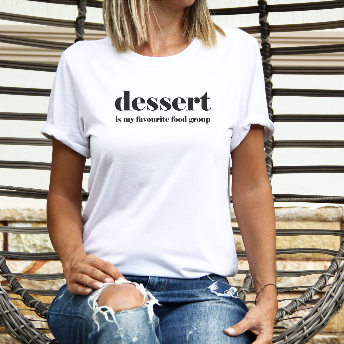 Person wearing a white t-shirt with 'dessert is my favourite food group' text, sitting on a wicker chair.