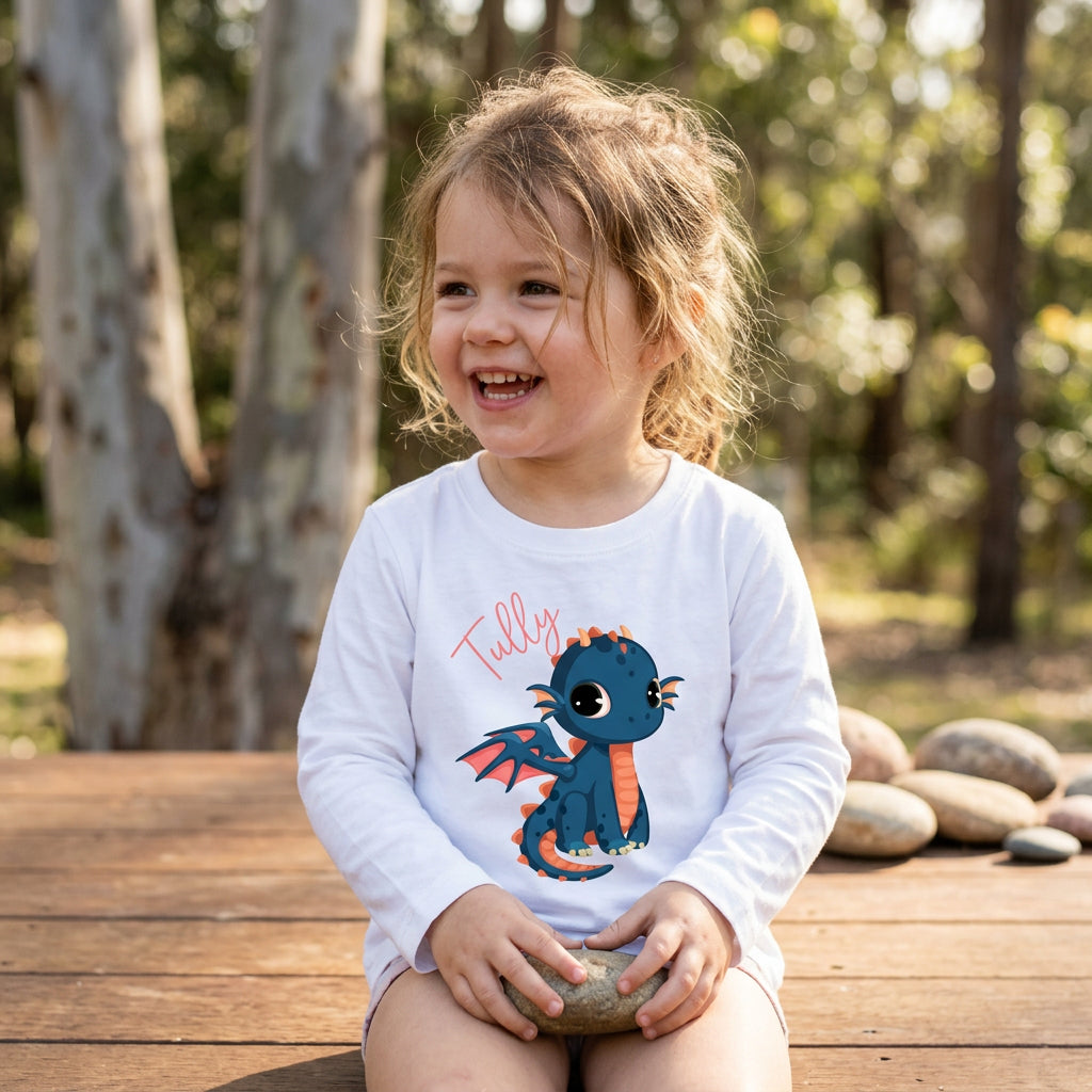 A white long-sleeve t-shirt with a graphic of a cute blue dragon with orange accents and the name 'Tully' written in pink script.
