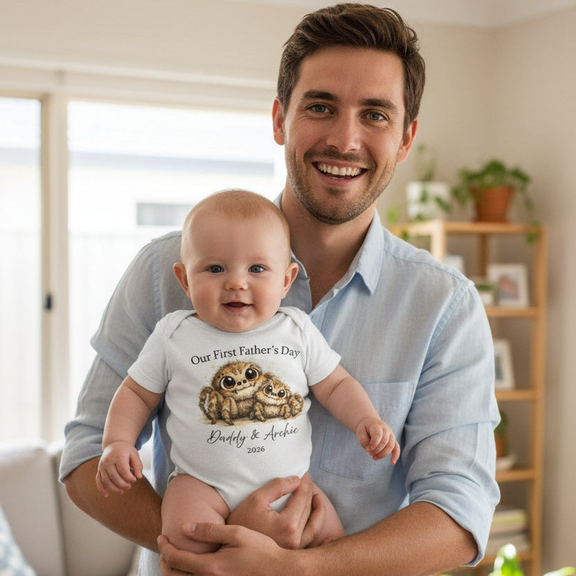 Baby wearing a white bodysuit with two huntsman spiders and Our First Father's Day text