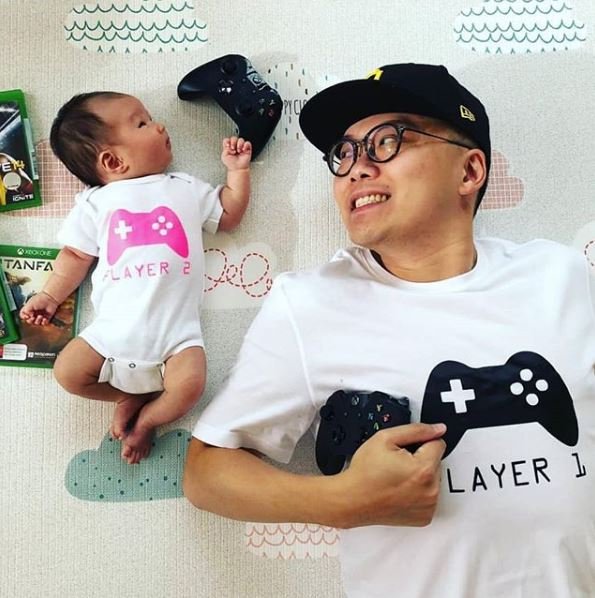 Dad and baby in matching white tops with controller designs reading Player 1 and Player 2.