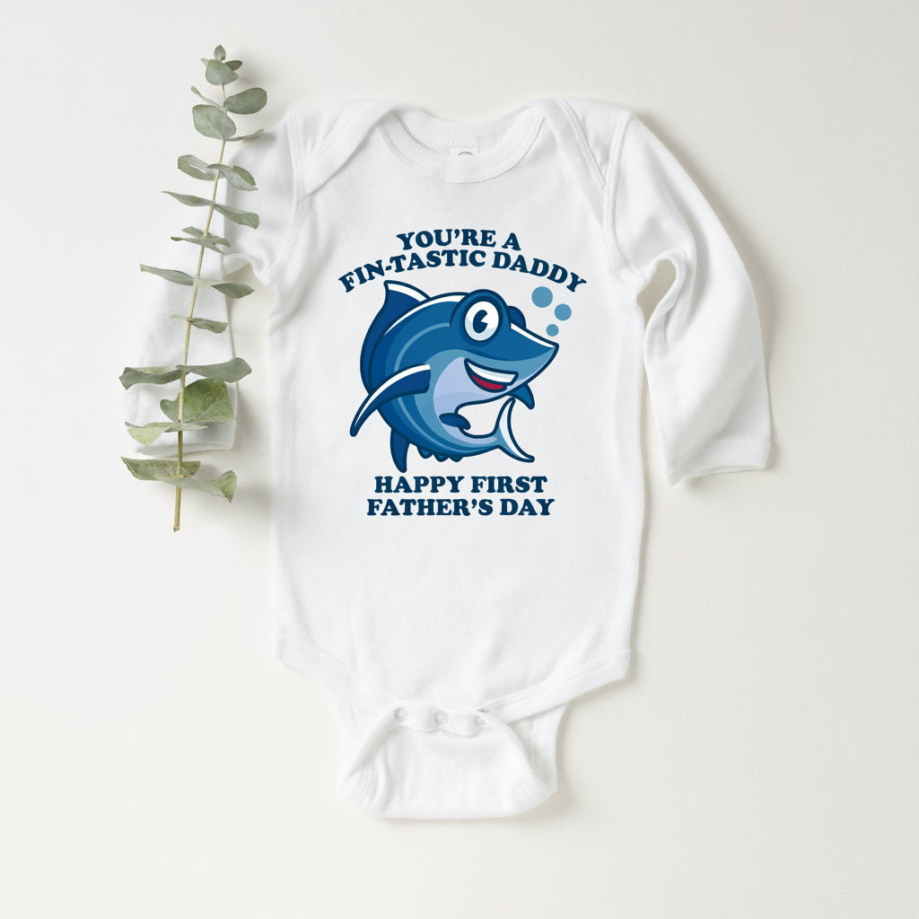 White baby bodysuit with a cartoon shark and text reading You're A Fin-Tastic Daddy, Happy First Father's Day.