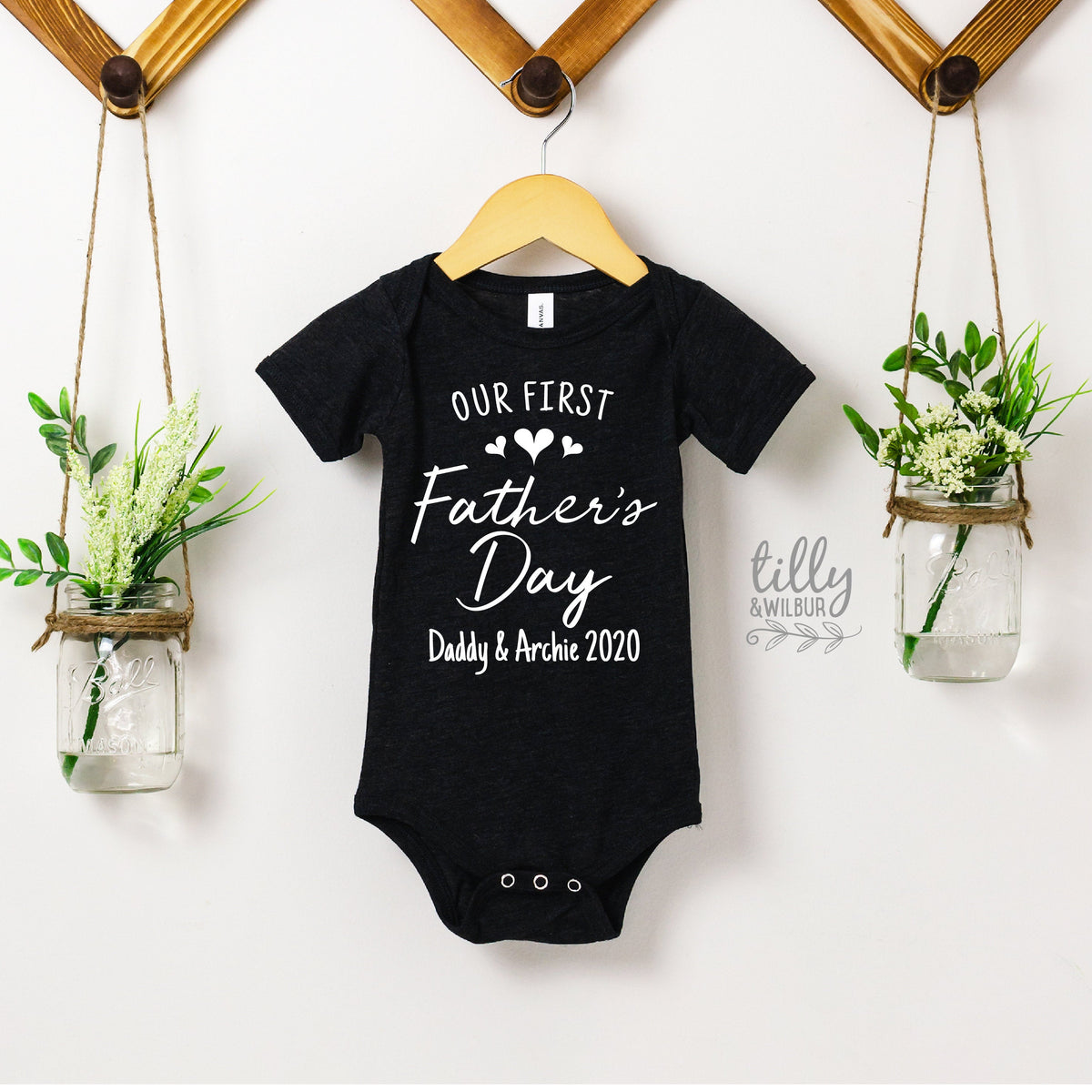 Black short-sleeve baby bodysuit with Our First Father's Day script and personalised names and year.