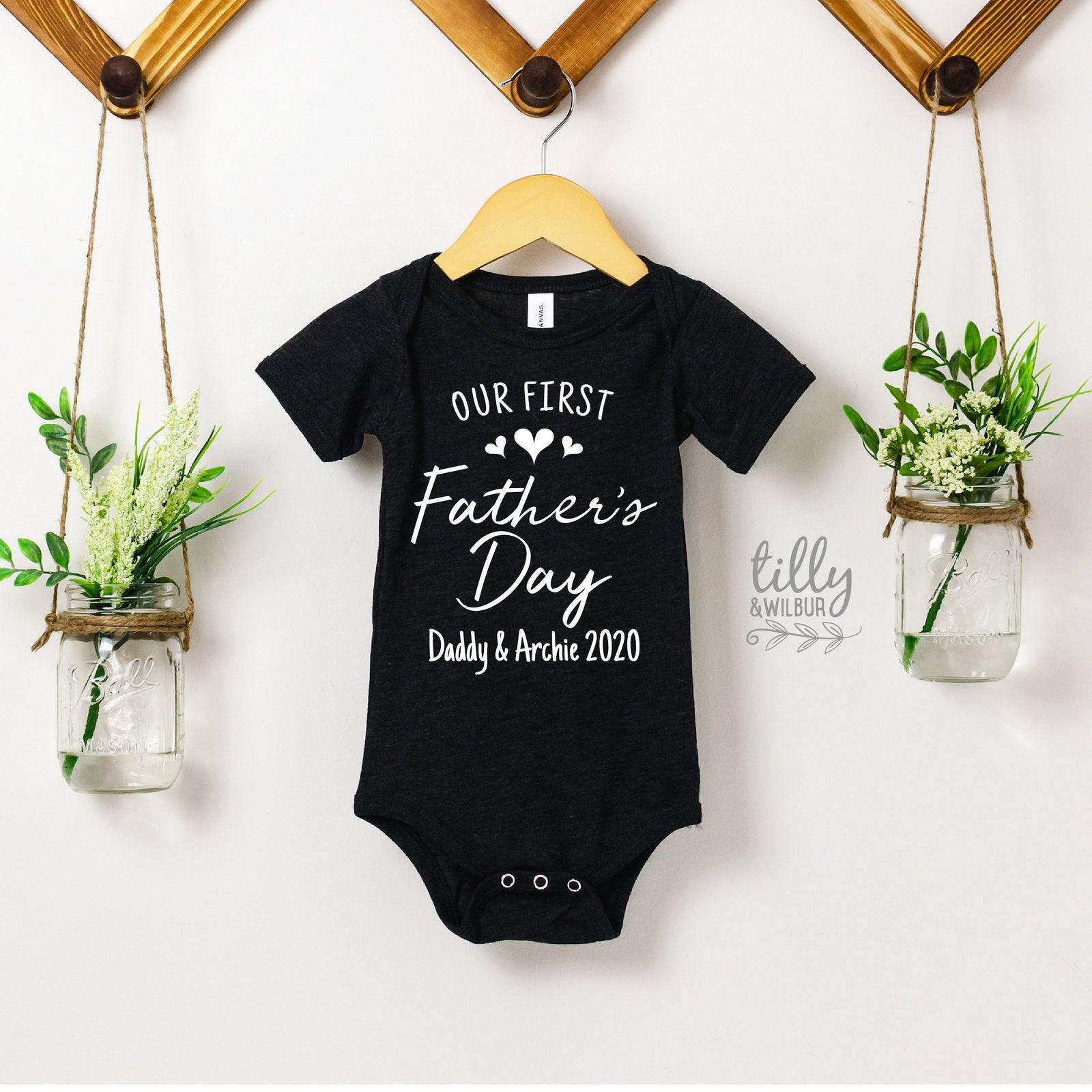 Black short-sleeve baby bodysuit with Our First Father's Day script and personalised names and year.