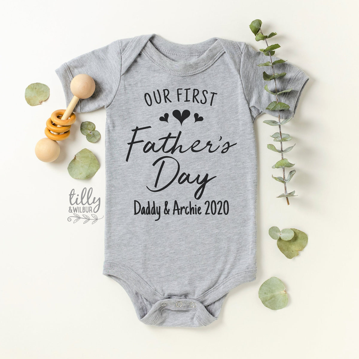 Grey short-sleeve baby bodysuit with Our First Father's Day script and personalised names and year.