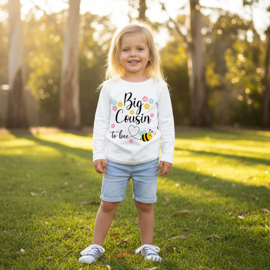 Smiling young girl wearing a white Big Cousin To Bee t-shirt with bee and flowers design, with her pregnant aunty in the background