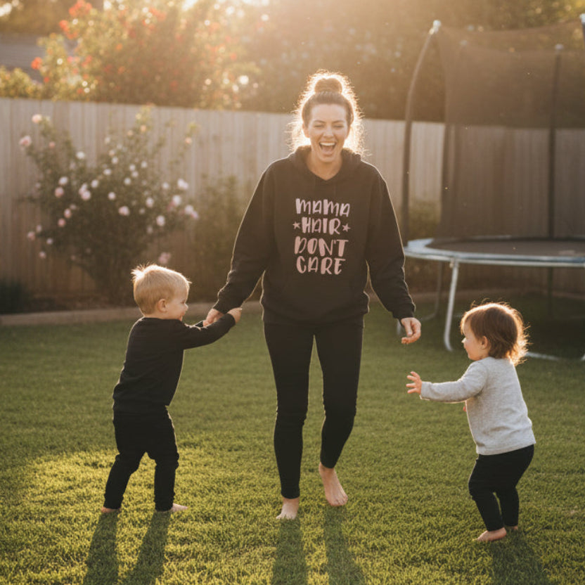 Black t-shirt with 'Mama Hair Don't Care' text in pink on a hanger against a blurred natural background.