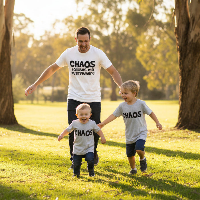 White t-shirt reading Chaos Follows Me Everywhere besidetwo grey kids t-shirts reading Chaos.