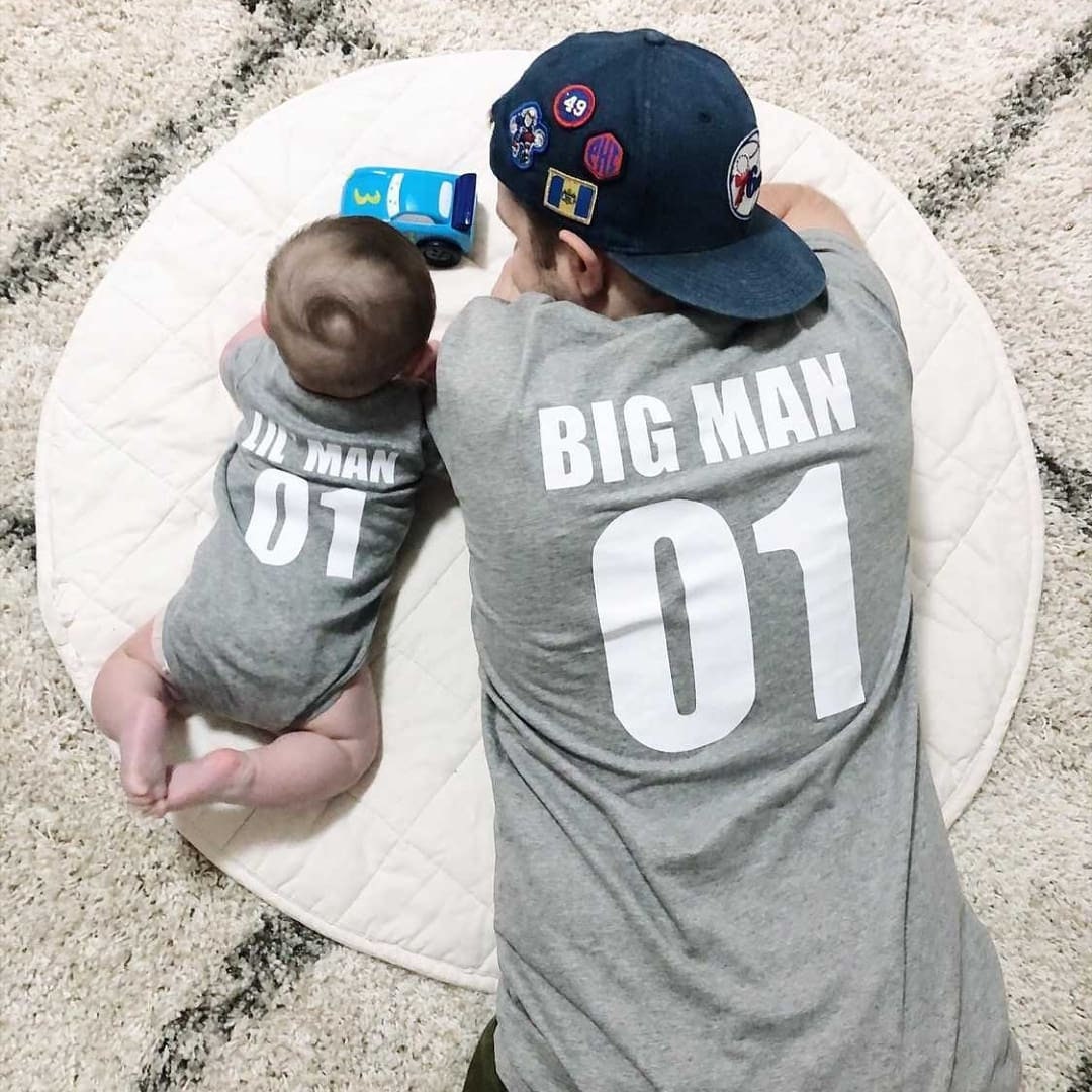 Dad and baby lying down in matching grey garments with Big Man and Lil Man number designs on the back.