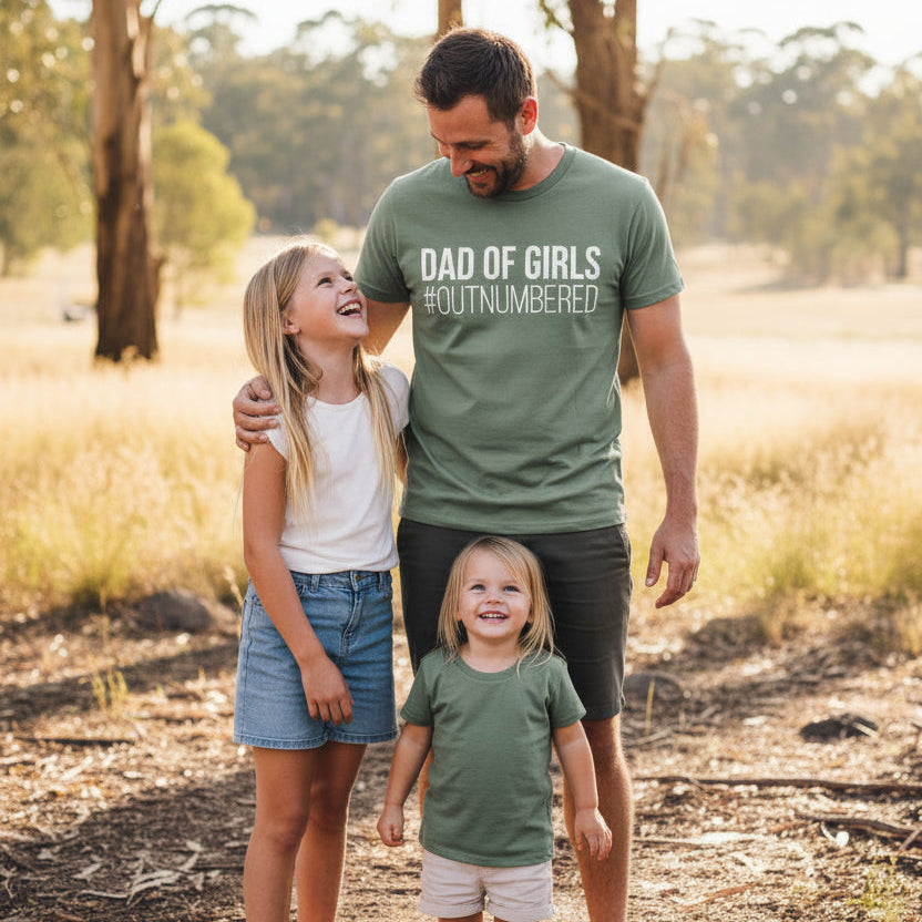 green t-shirt with bold white text reading Dad Of Girls #Outnumbered.