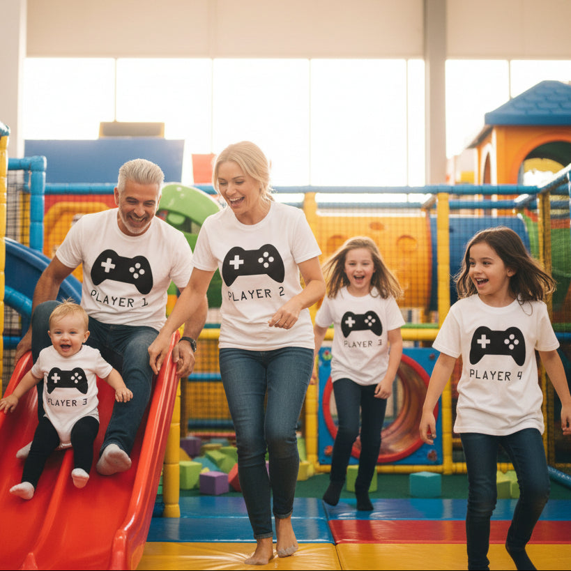 Family of five wearing matching t-shirts with 'Player' text and game controller graphics outdoors.