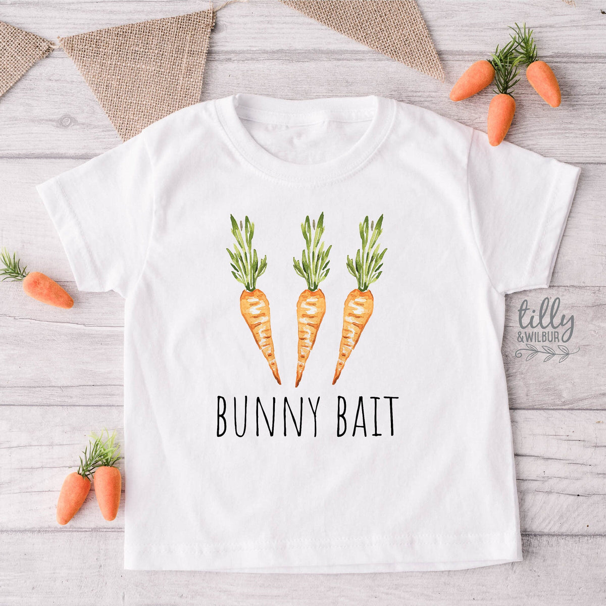 White t-shirt with carrot design and 'Bunny Bait' text on a wooden surface with decorative carrots.