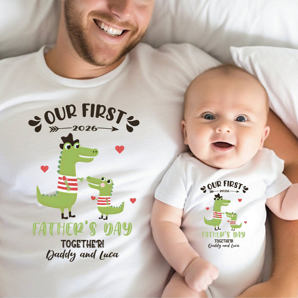 A smiling man and a baby lying together on a white bed, both wearing matching white graphic t-shirts and bodysuits printed with a green crocodile illustration, hearts, and the text 'OUR FIRST 2026 FATHER'S DAY TOGETHER! Daddy and Luca'.