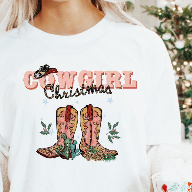 A woman holding a mug and wearing a white t-shirt with 'COWGIRL CHRISTMAS' text and a graphic of cowboy boots and a Christmas tree.