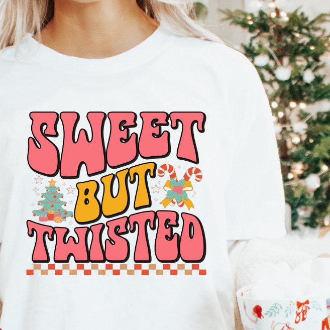 A person holding a mug and wearing a white long-sleeve T-shirt with the text 'SWEET BUT TWISTED' printed on the front, along with the taglines 'Baby, Kids &amp; Adults'.