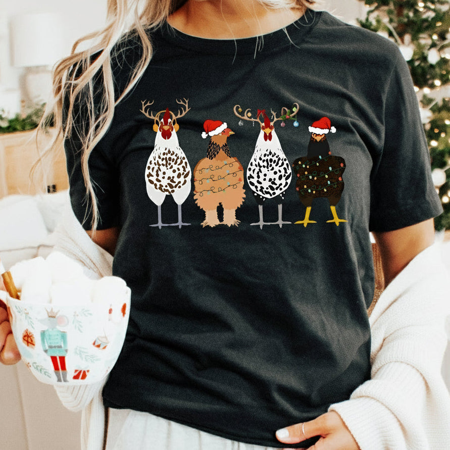 A black t-shirt with a graphic of four cartoon chickens wearing Santa hats and Christmas-themed decorations in the background.